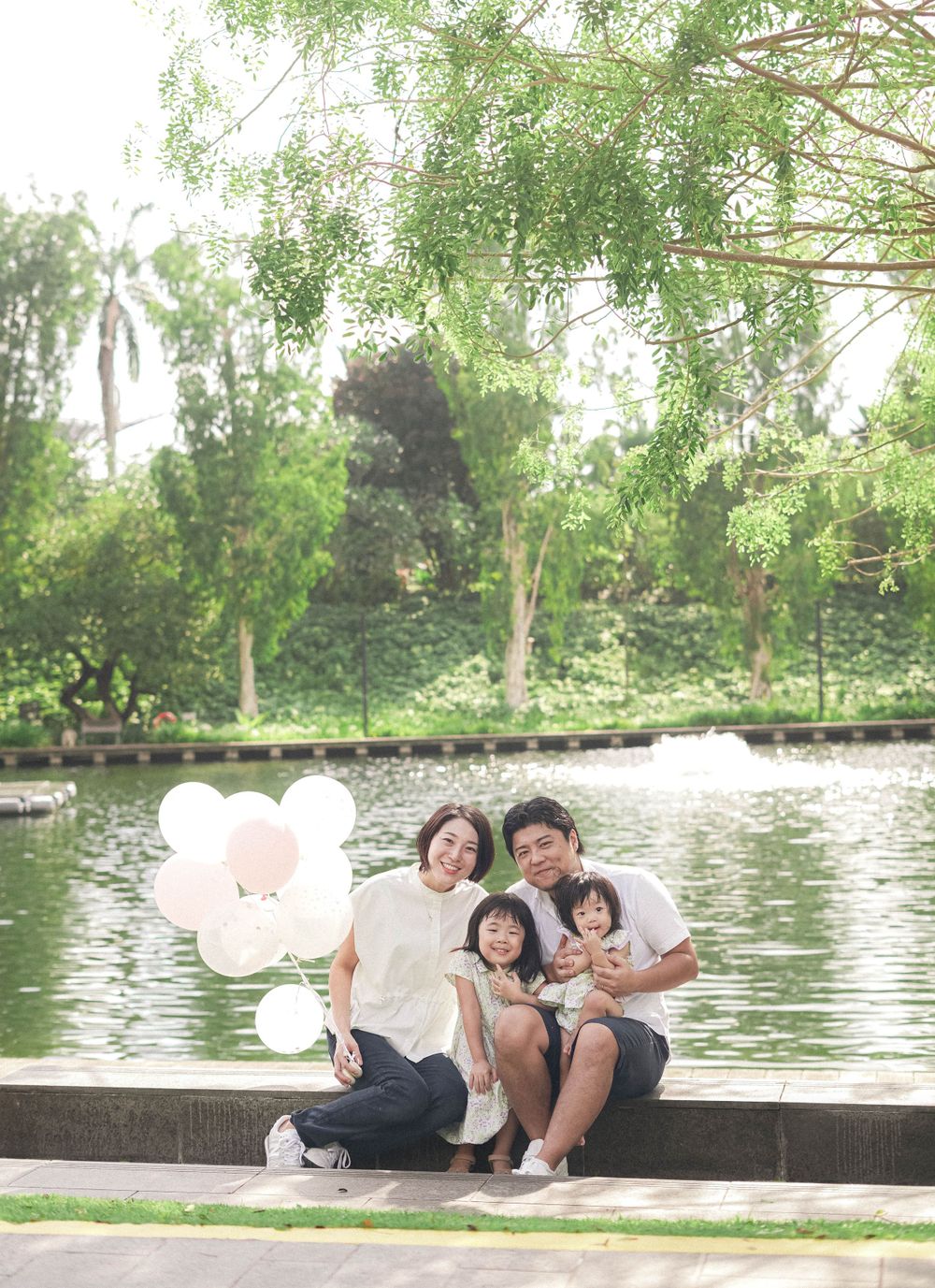 Family sitting by lake with white balloons during outdoor photo session.