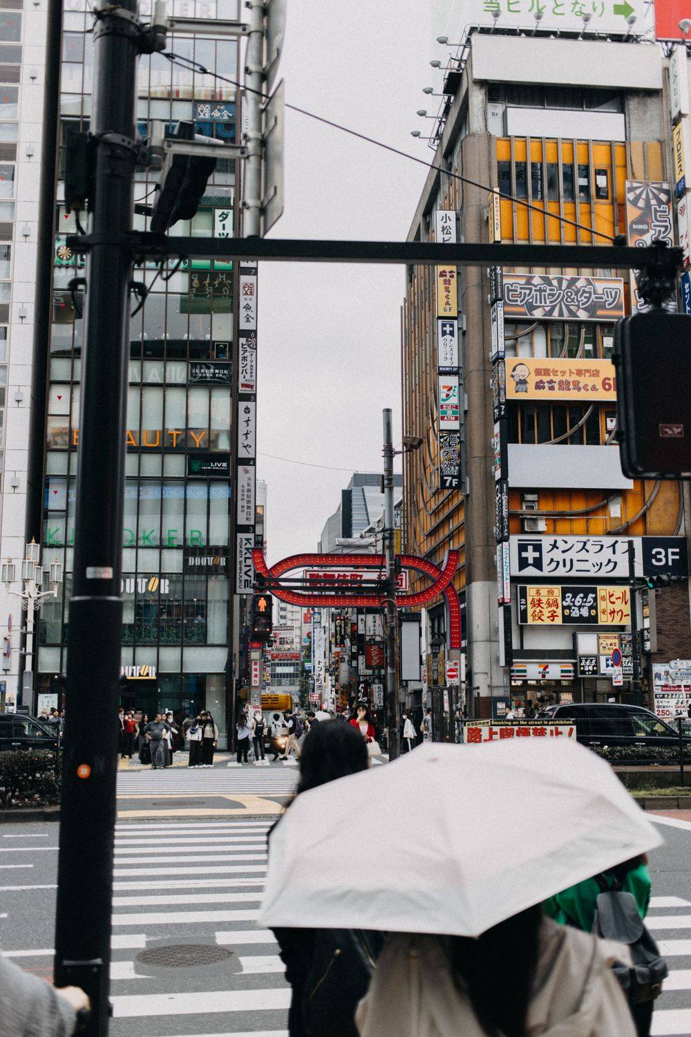 Rainy Tokyo street scene with modern buildings and pedestrians holding umbrellas.