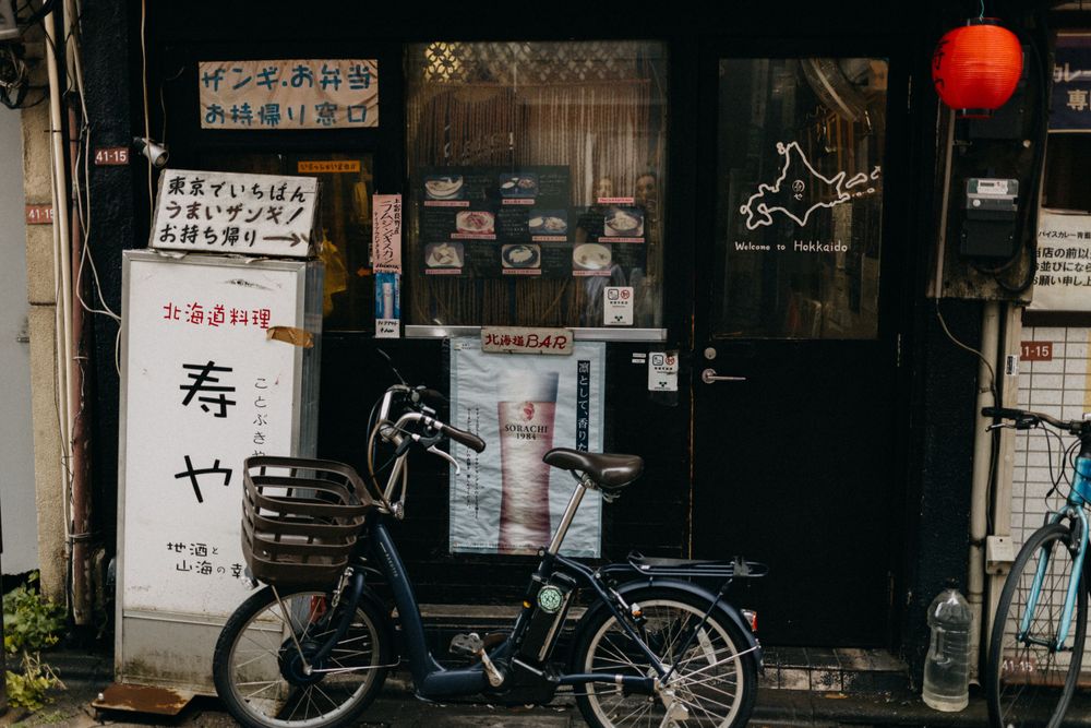 Dark alley with a parked bicycle and Japanese text signs on building facade.