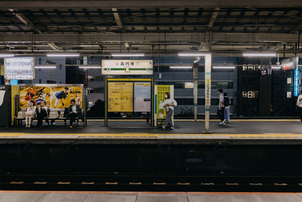 Japanese train station platform with yellow safety line and waiting passengers.