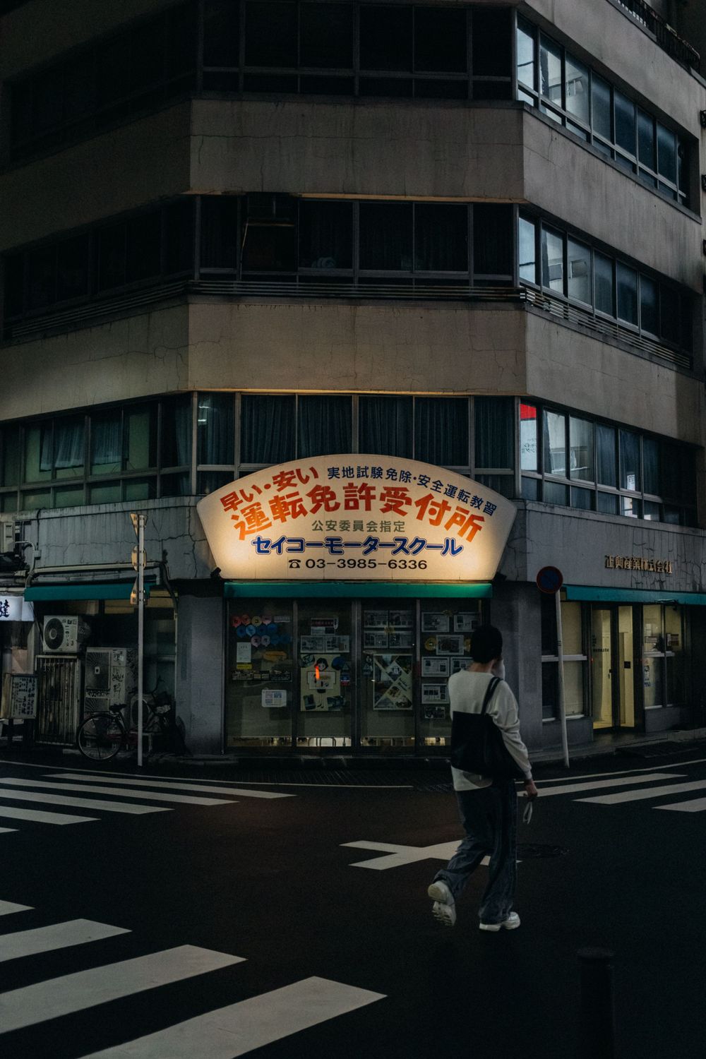 Corner building with Japanese text signage and crossing pedestrian at dusk.