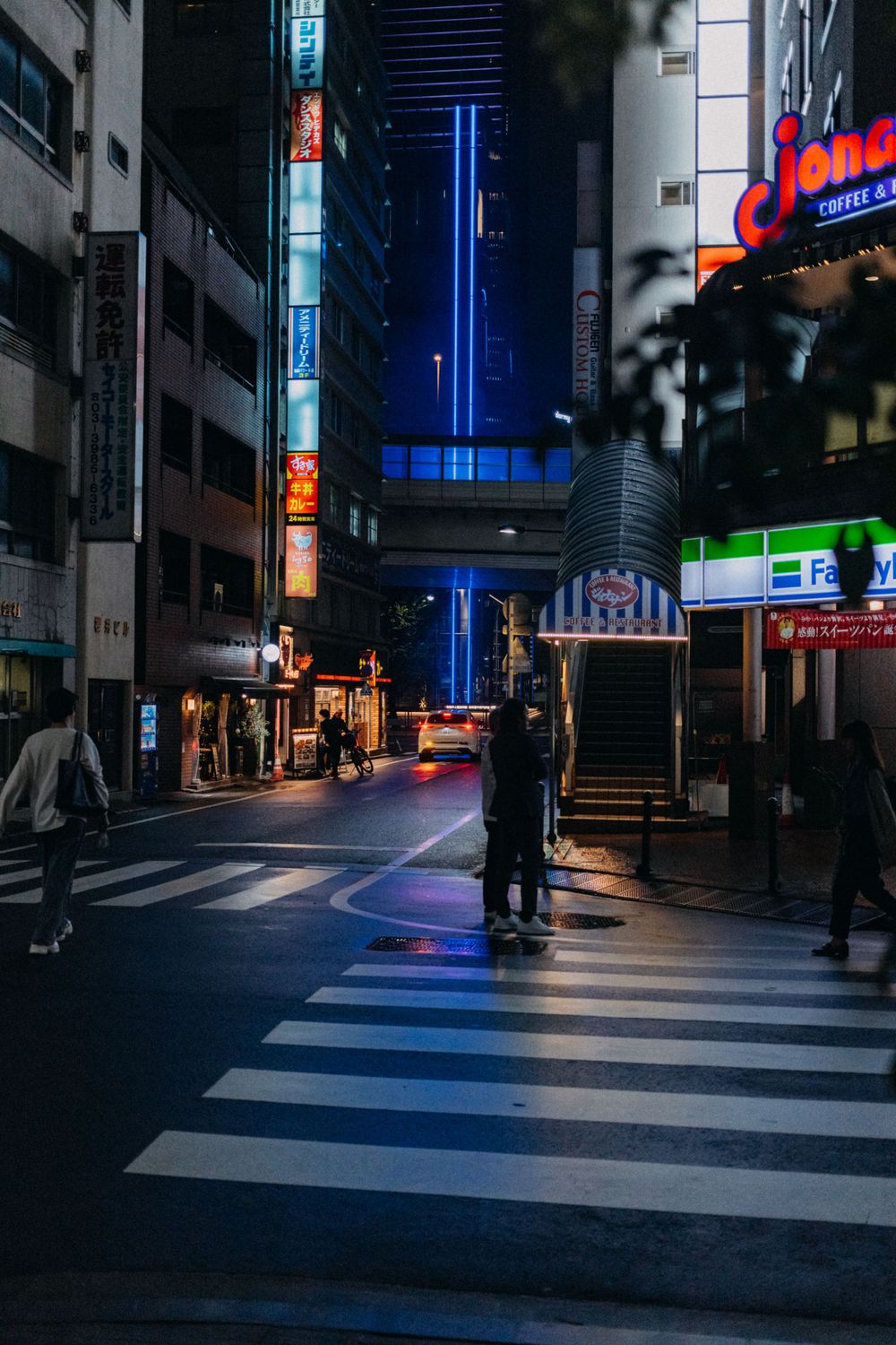 Moody nighttime street scene in Tokyo with neon blue lights and a zebra crossing.