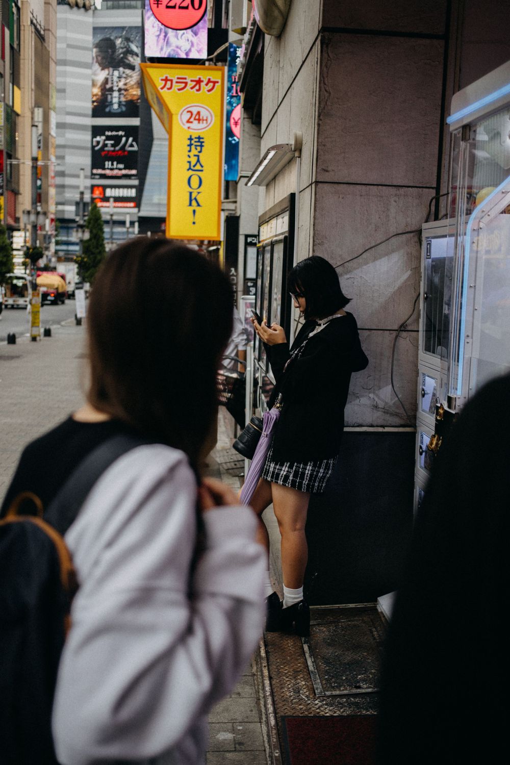Street scene in Japan with karaoke signs and pedestrians on a city sidewalk.