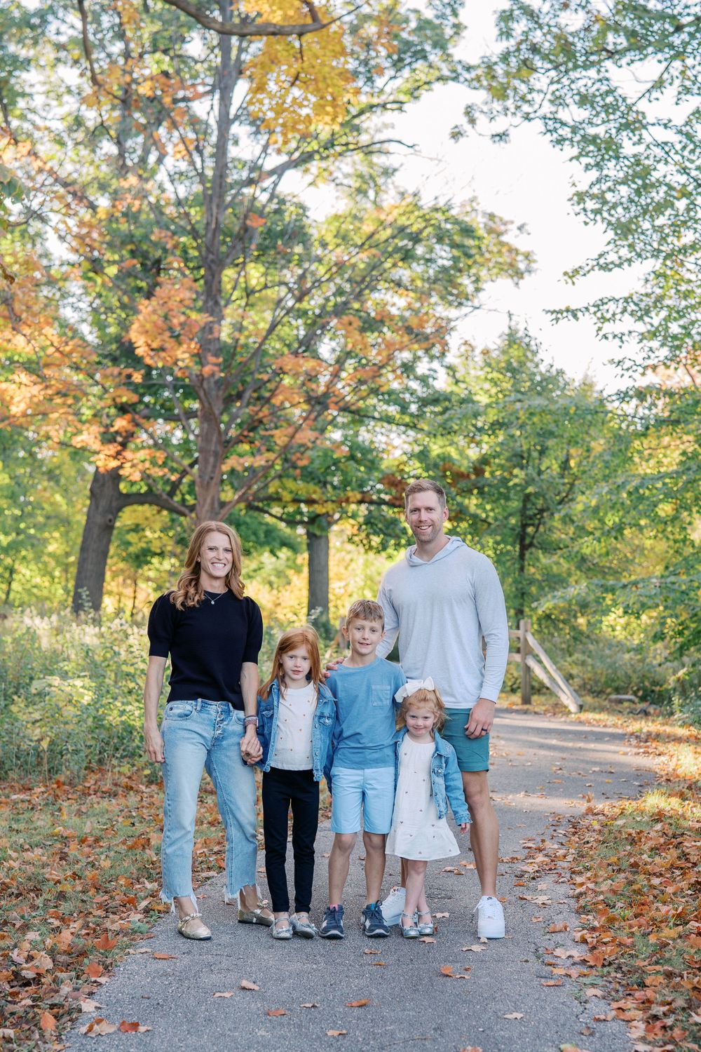 A family portrait taken on a wooded path with fall foliage in the background.