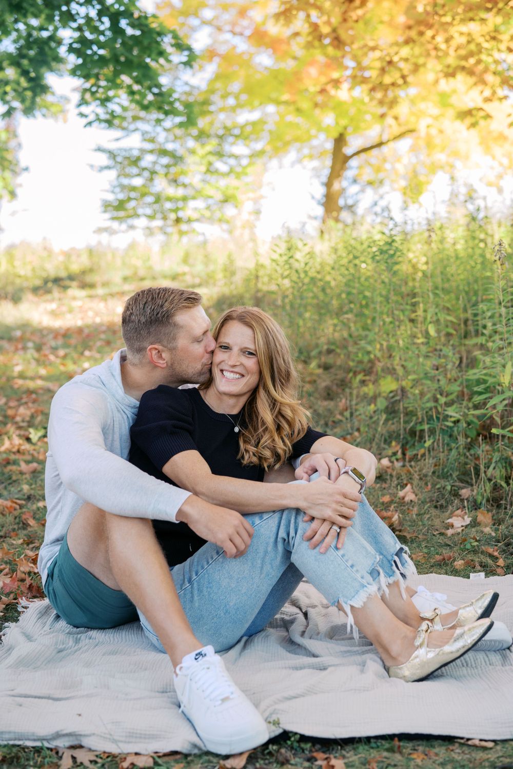 Couple shares intimate moments during outdoor photo session on blanket.