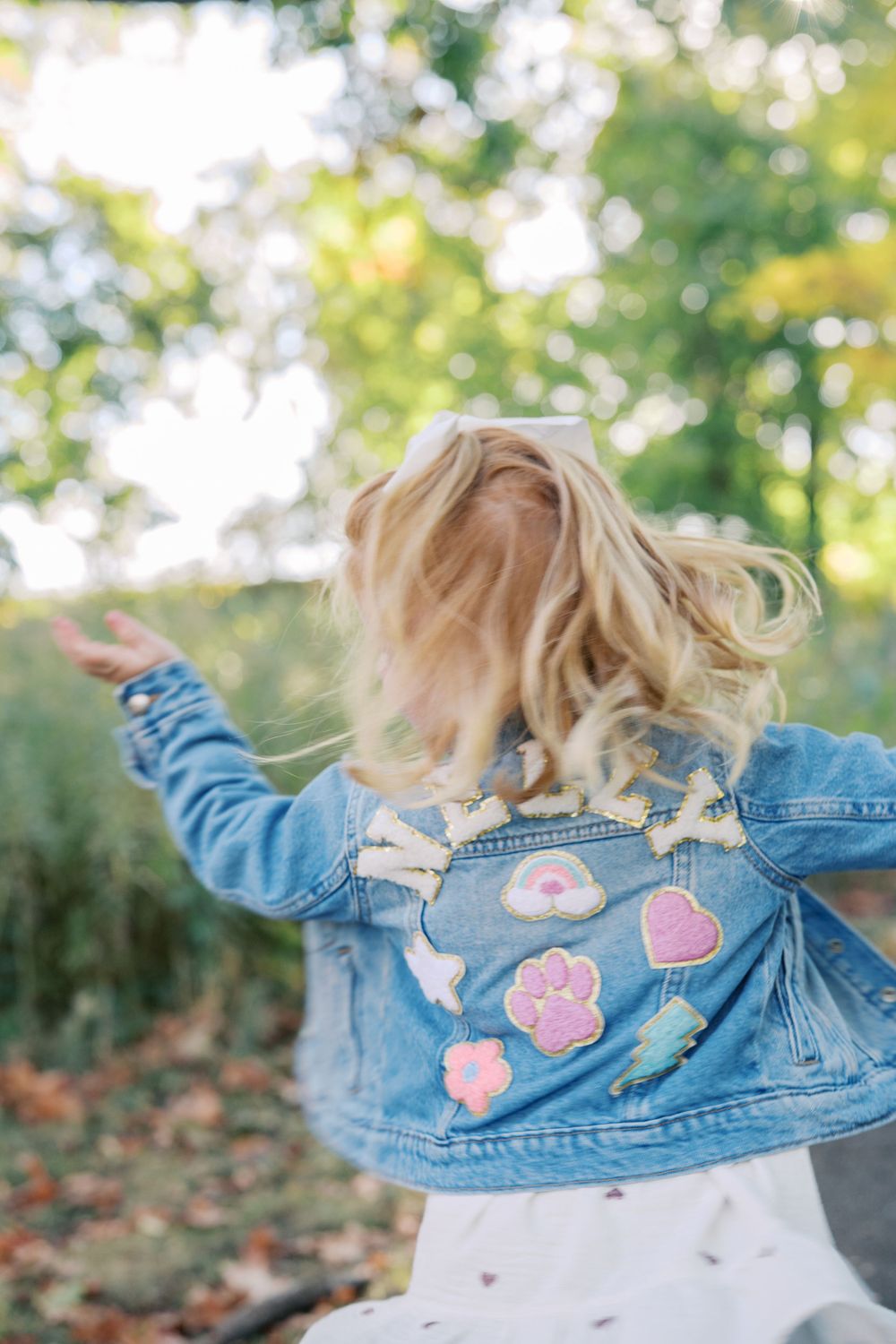 Denim jacket with pink heart patches shown in motion against fall foliage.