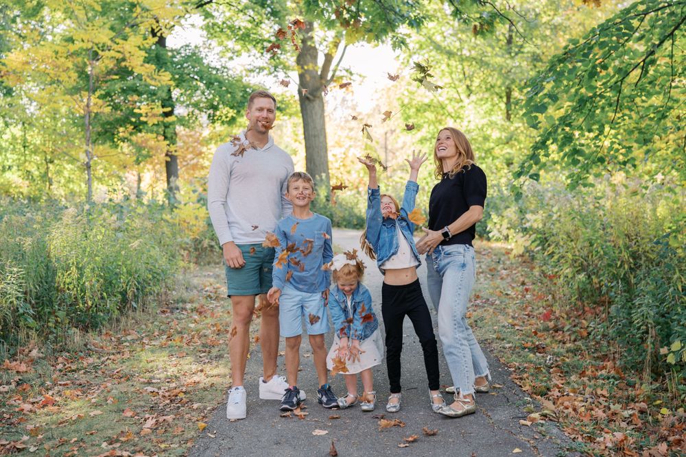 A playful autumn photoshoot on a tree-lined path with fallen leaves scattered on the ground.