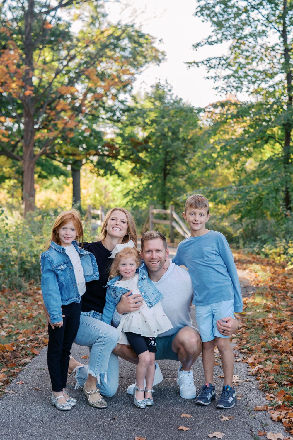 Family poses together on a scenic autumn path surrounded by colorful fall foliage.