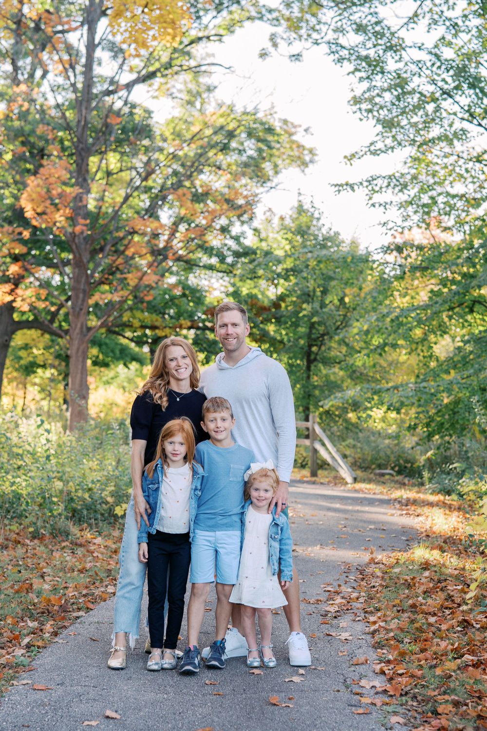 A family group stands together on a leaf-covered path during autumn.
