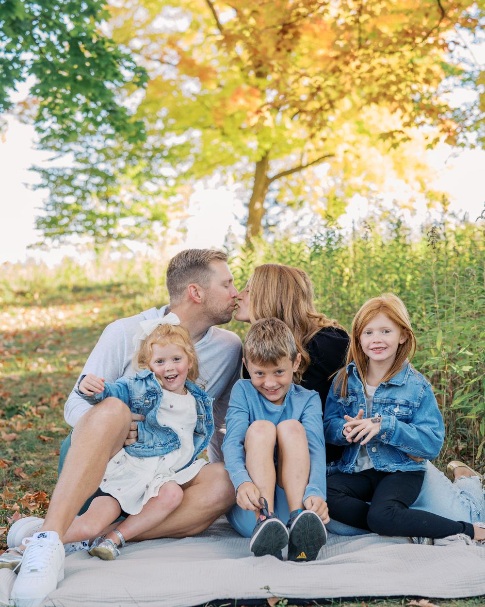 Family members wearing coordinated denim outfits share loving moments on a blanket in nature.