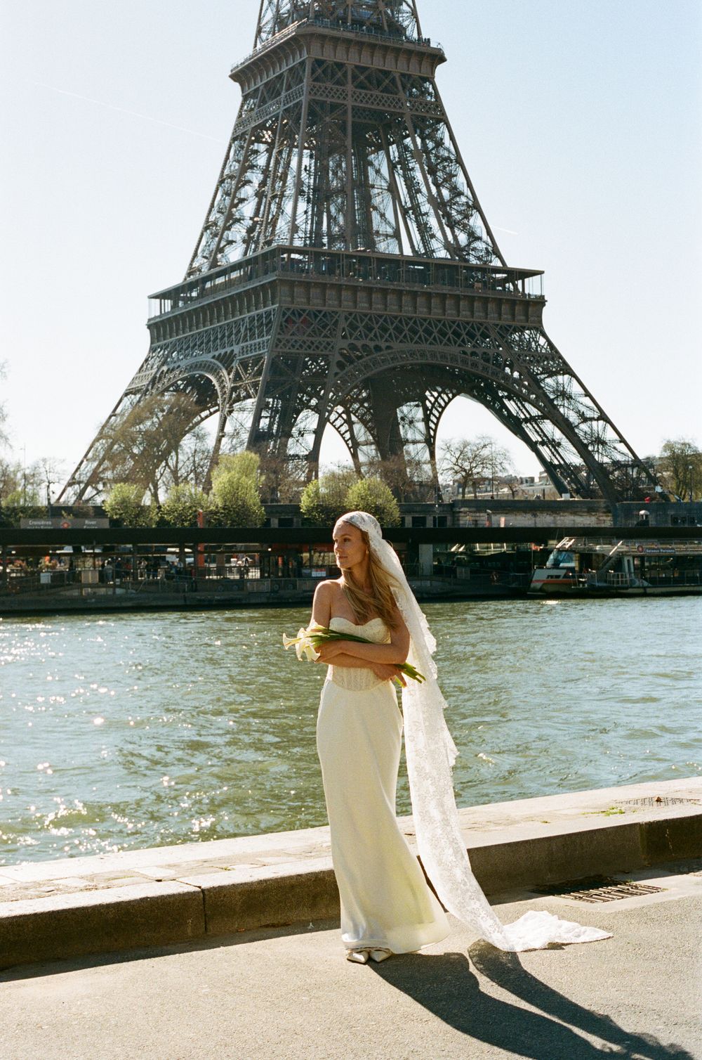 Bride in white gown and veil posing by the Seine River with the Eiffel Tower in Paris, France.