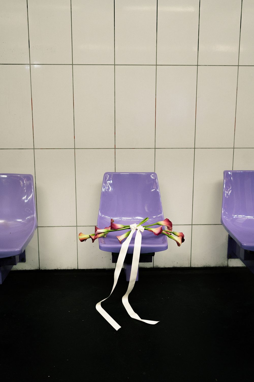 Purple plastic chairs with calla lilies tied with white ribbon on center seat against white tiled wall.