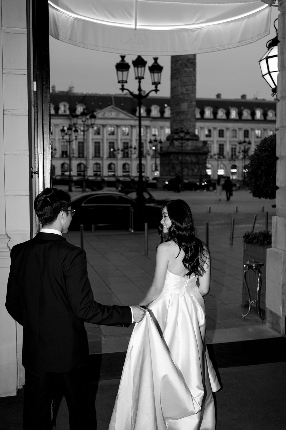 Black and white photo of a bride and groom holding hands at Place Vendôme Paris at dusk.