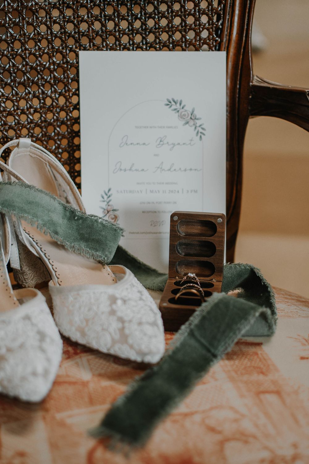 Elegant wedding invitation with delicate floral design displayed alongside white lace shoes and sage green velvet ribbon.