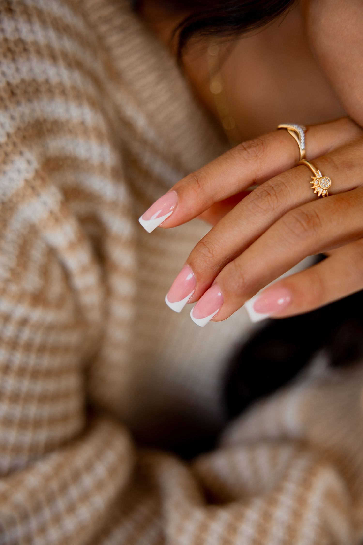 Close-up of French manicured nails and delicate gold rings on woman's hand.