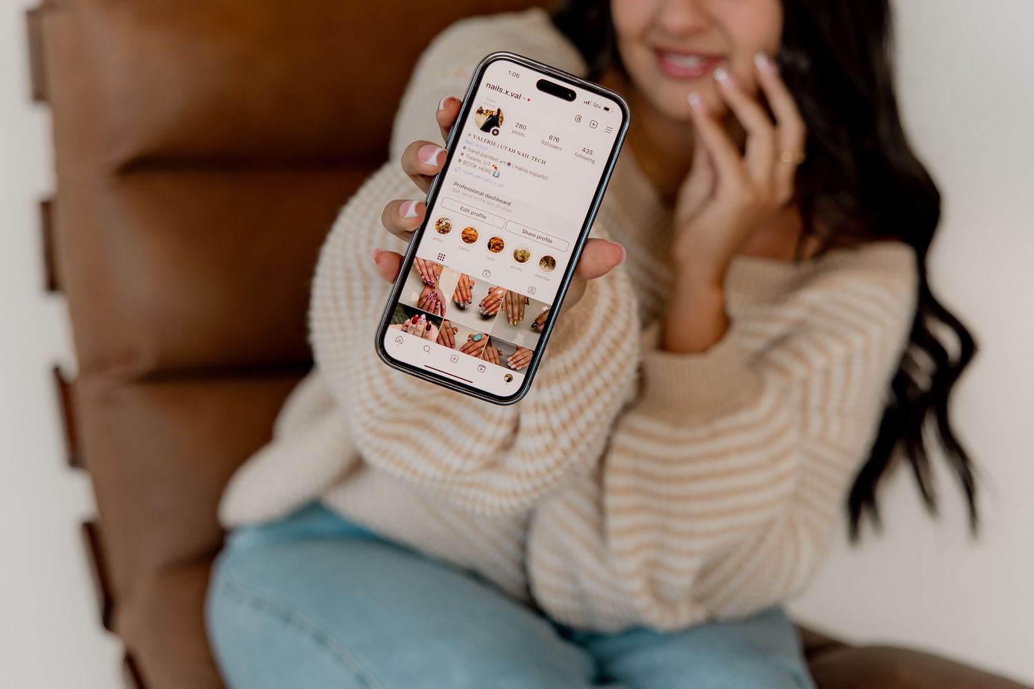 Person in cream sweater holding phone displaying social media feed.