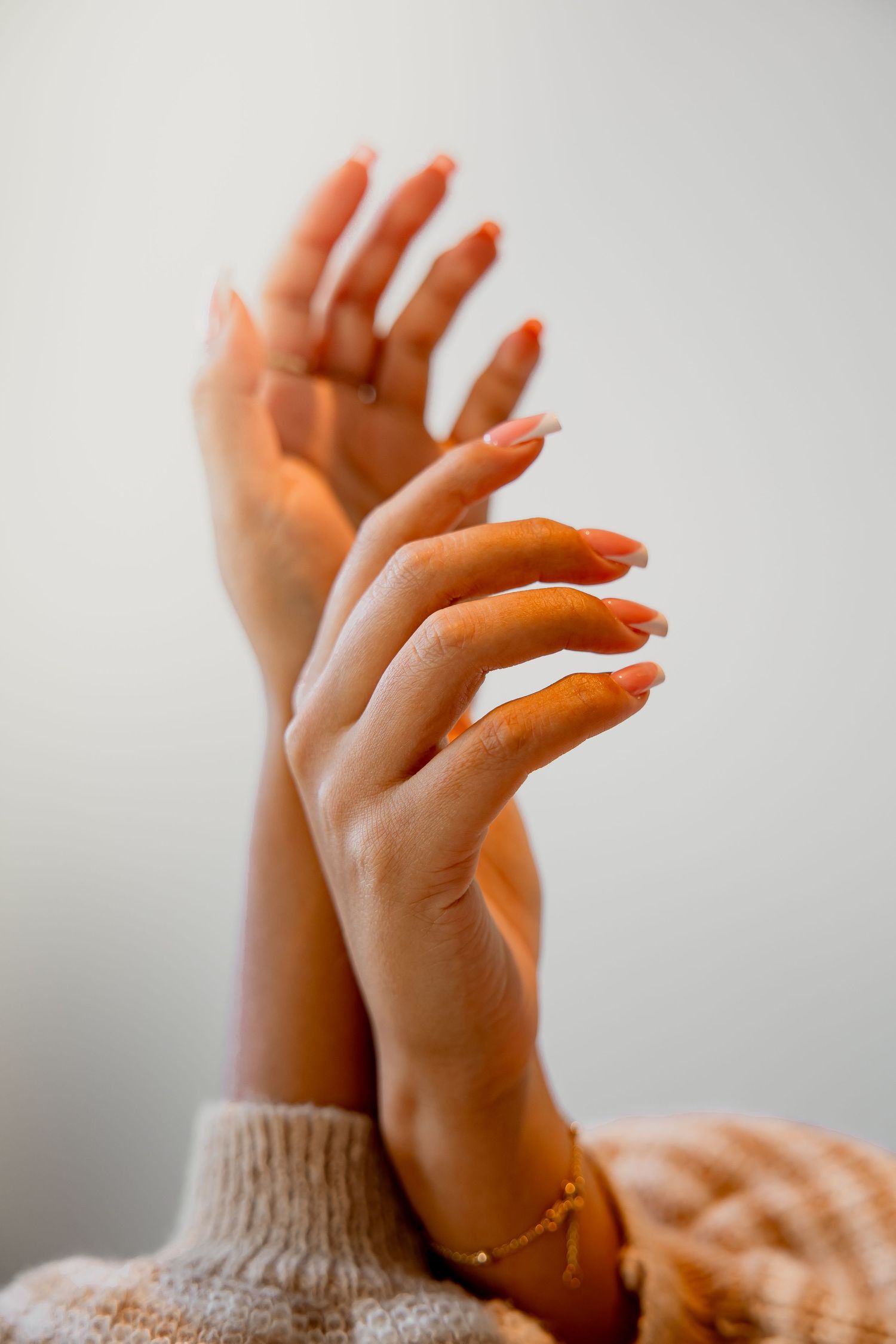 Elegant hands with manicured nails gracefully posed against beige sweater background.