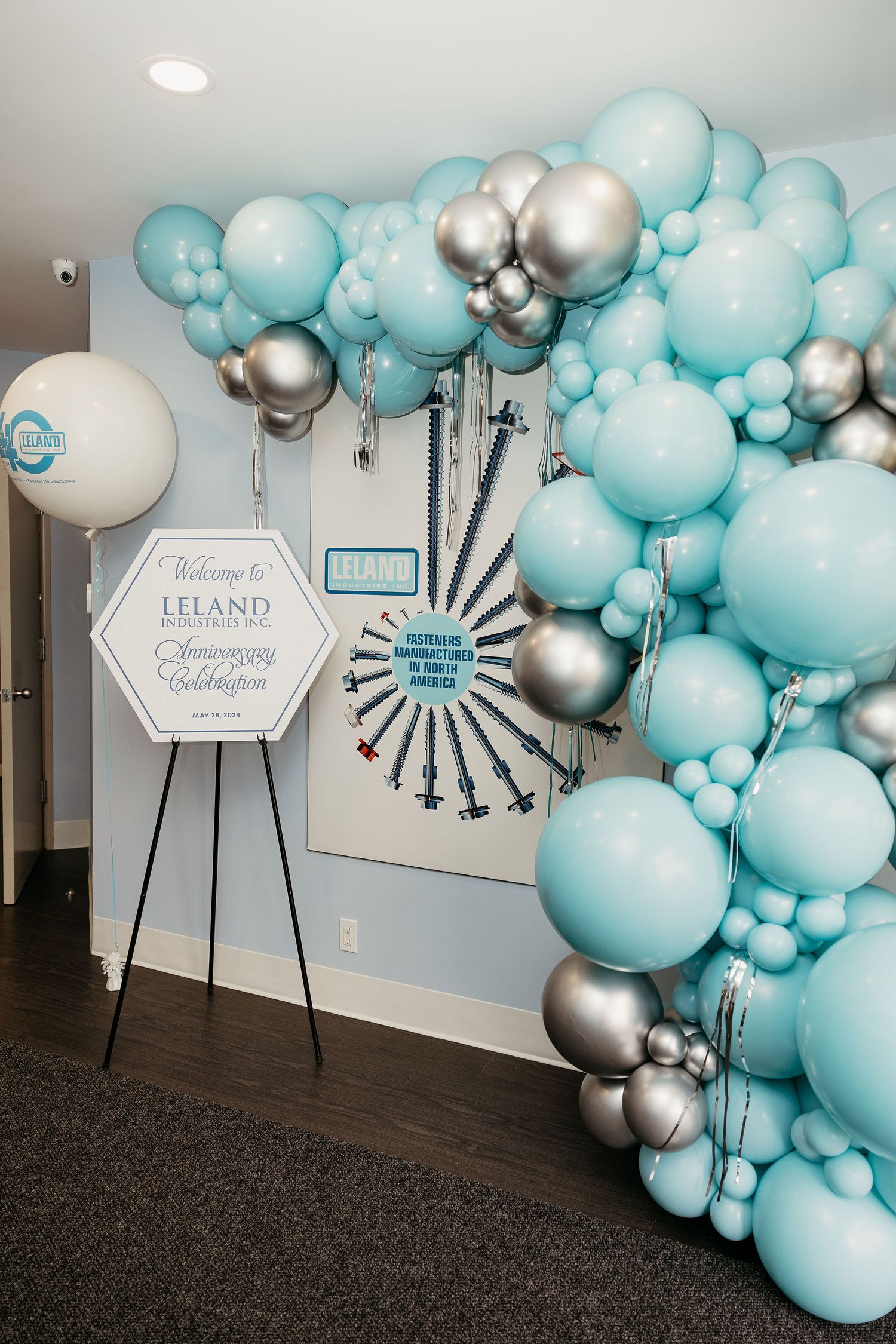 Elegant balloon arch in turquoise and silver colors with decorative signage for a corporate celebration.