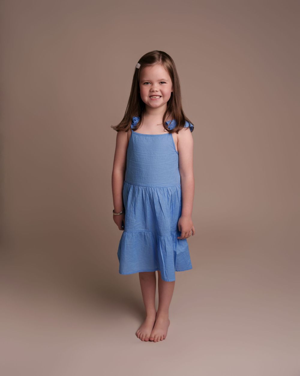 Girl in blue flutter sleeve dress stands barefoot against neutral studio background.