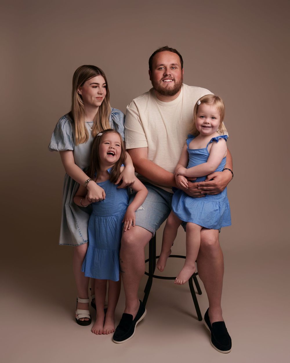 A family of four poses together for a studio portrait against a neutral brown background.