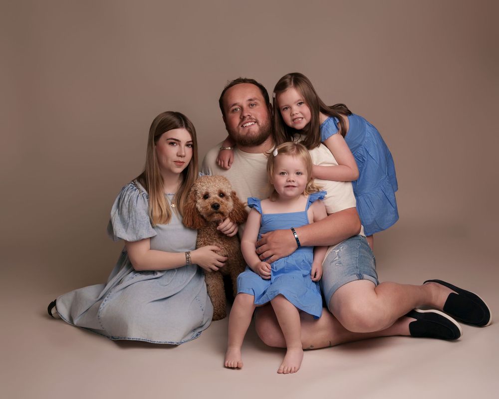 A family sits together with their golden-colored dog in a brown studio setting.