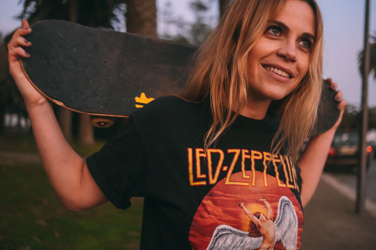 Person holding a skateboard wearing a vintage Led Zeppelin t-shirt at sunset.