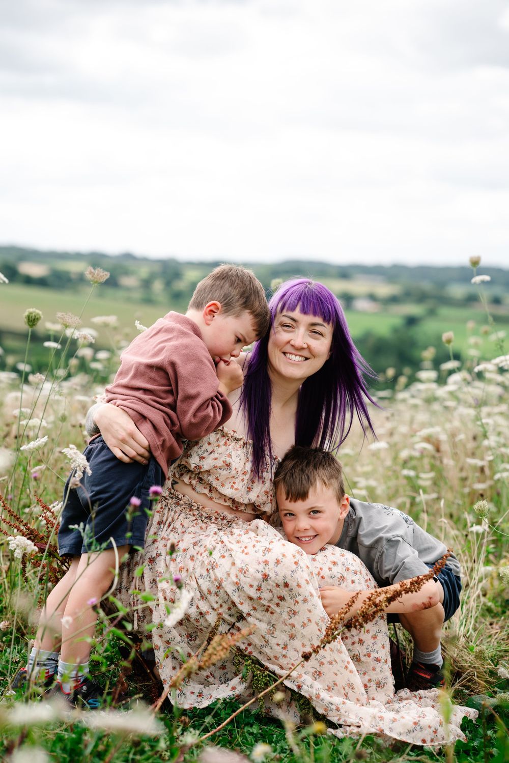 Family shares tender moments together while sitting in a blooming wildflower meadow on a sunny summer day.