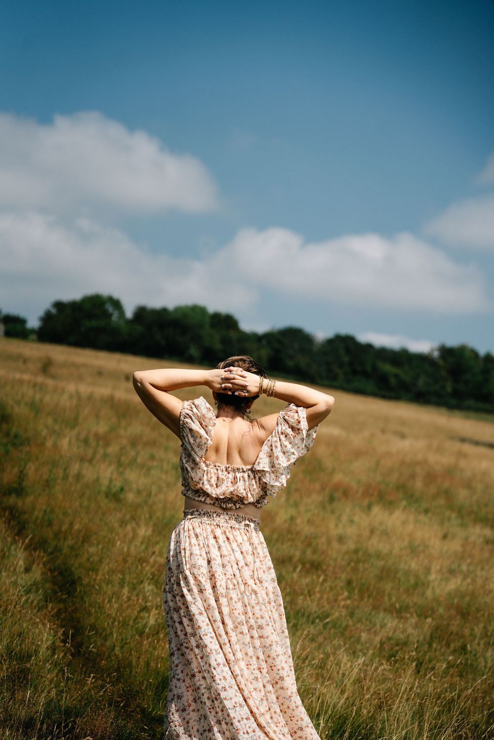 A flowing peach-colored dress moves gracefully against a backdrop of rolling hills and blue summer sky.