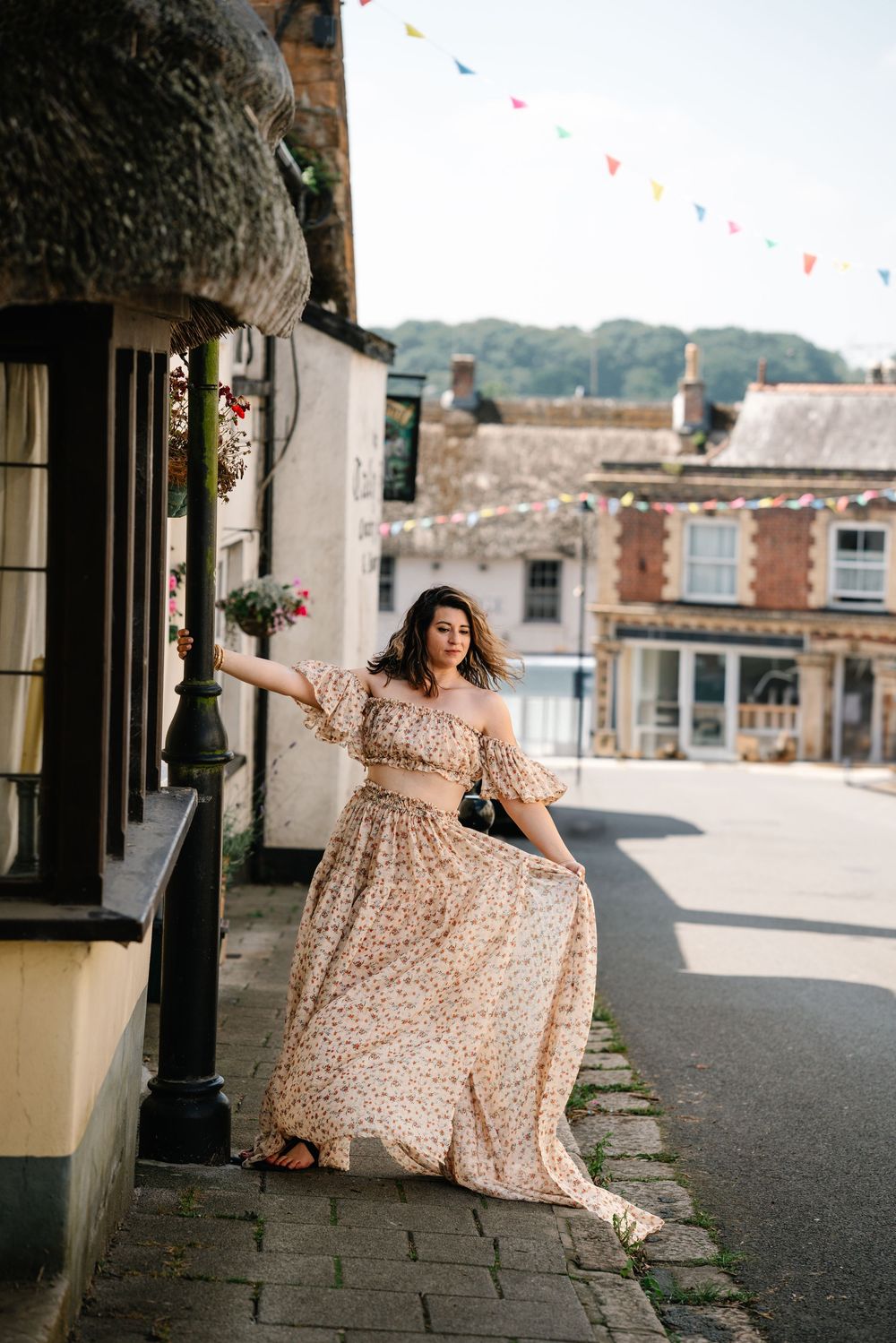 A person in a floral maxi dress poses gracefully on a stone walkway with city buildings visible in the background.