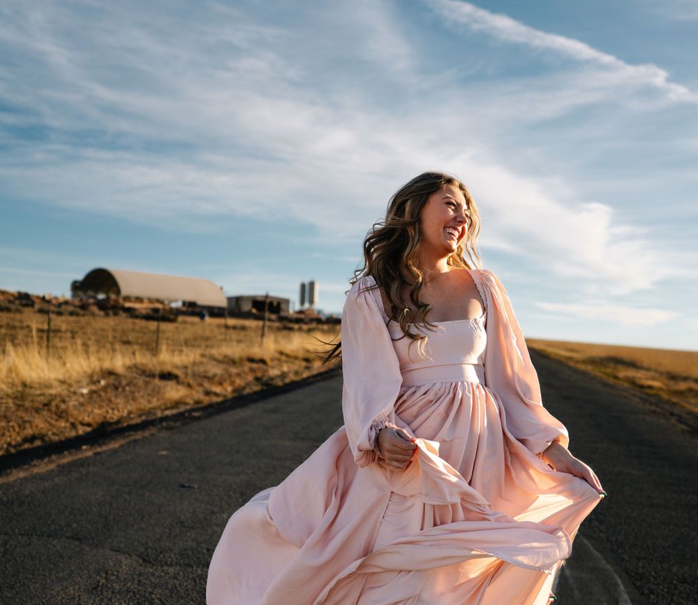 Pink dress billows in the wind on a rural road during golden hour.