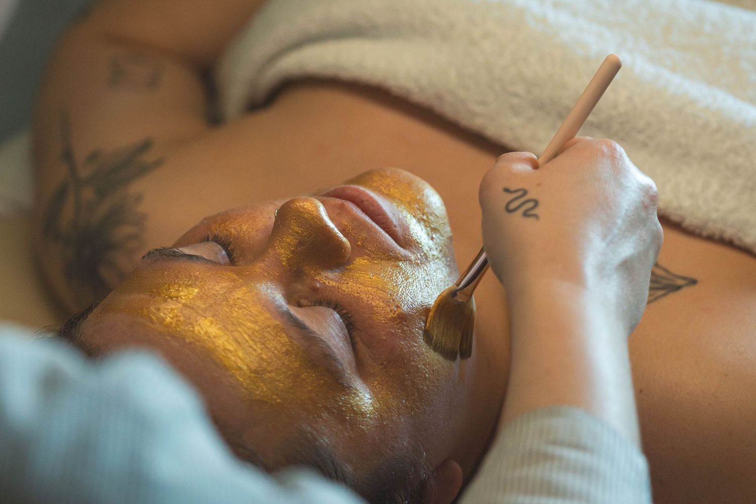 personal branding photography Brighton  of a massage therapist hands giving a gold facial to a woman lying down in a towel