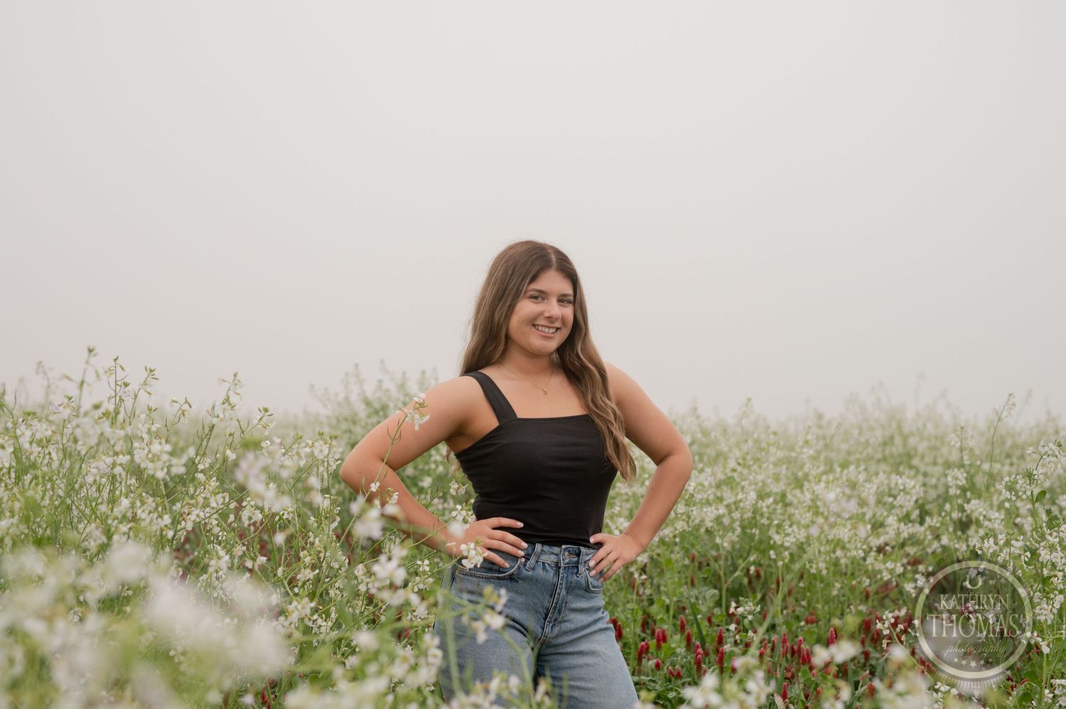 Confident pose in casual attire surrounded by blooming wildflowers and natural scenery.