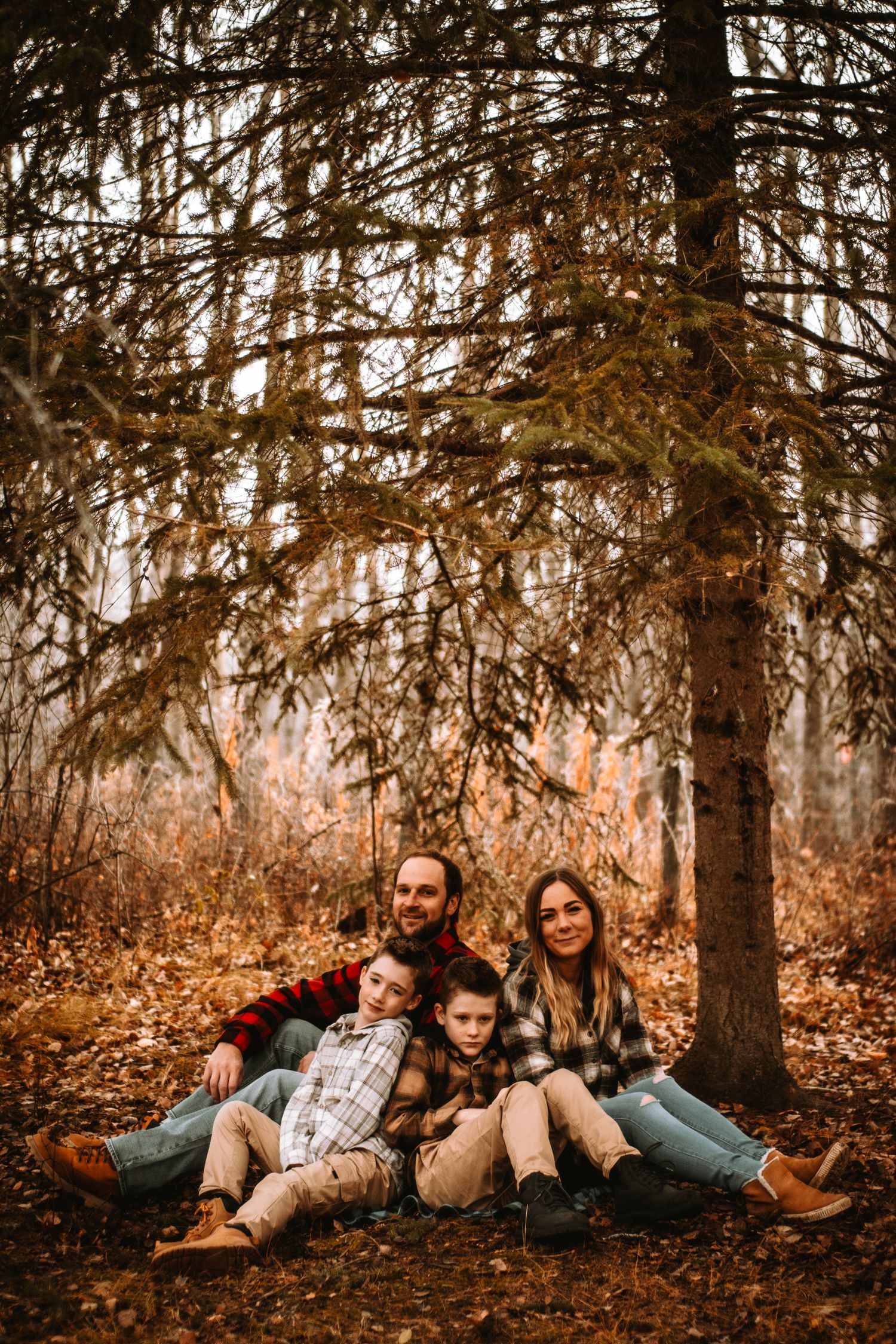 Autumn forest family portrait with tall evergreen trees and fallen leaves.
