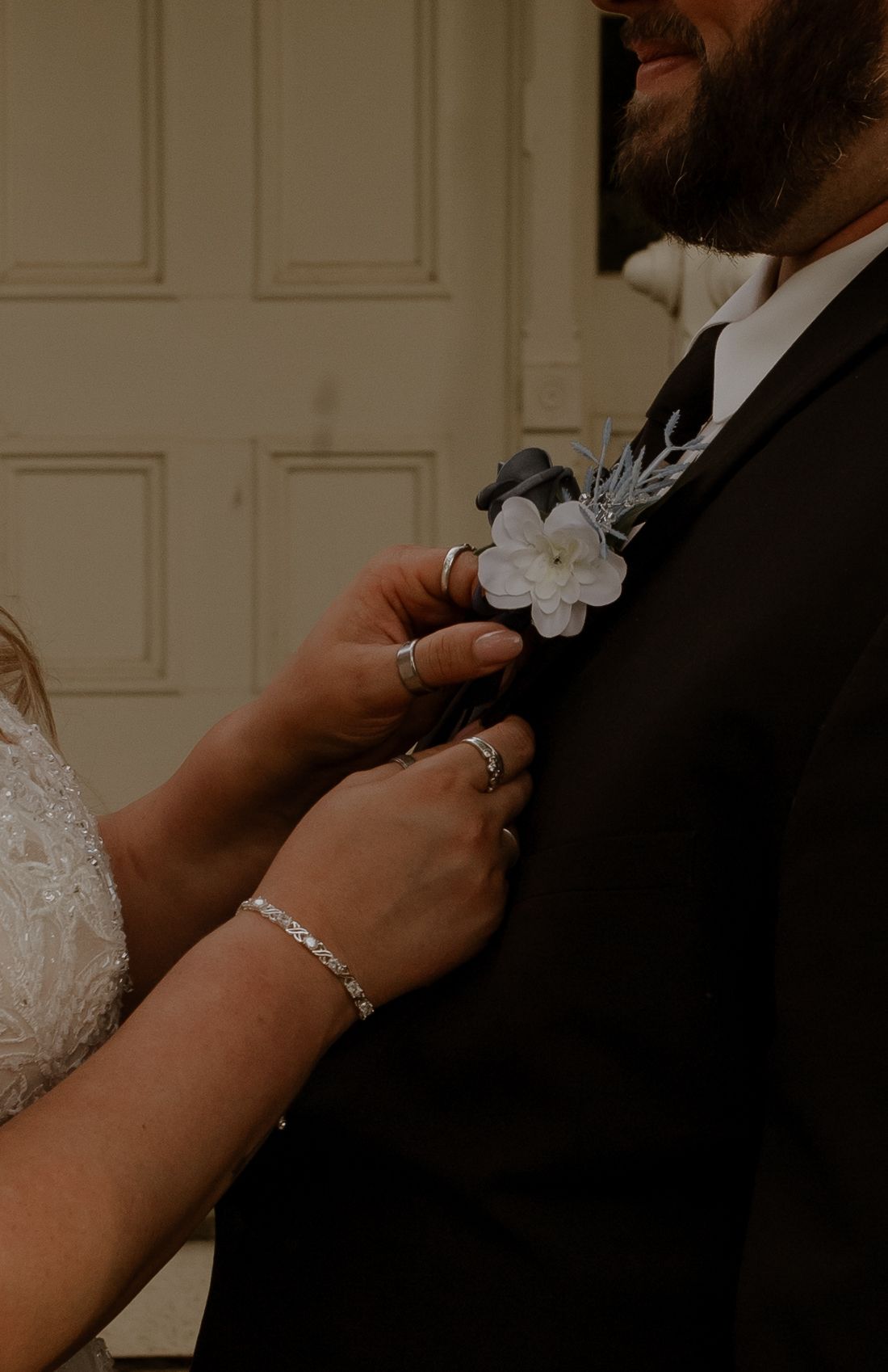 Close-up shot of hands adjusting a white boutonniere on a black suit jacket.