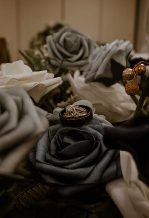 Black and white roses arranged with wedding rings nestled among the petals in moody lighting.