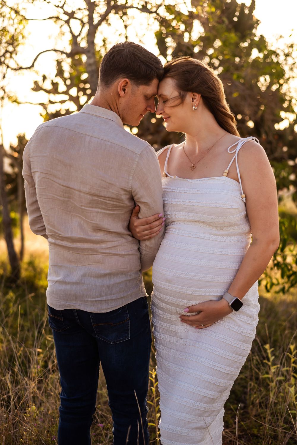 Romantic maternity photo of couple embracing in natural lighting during golden hour.