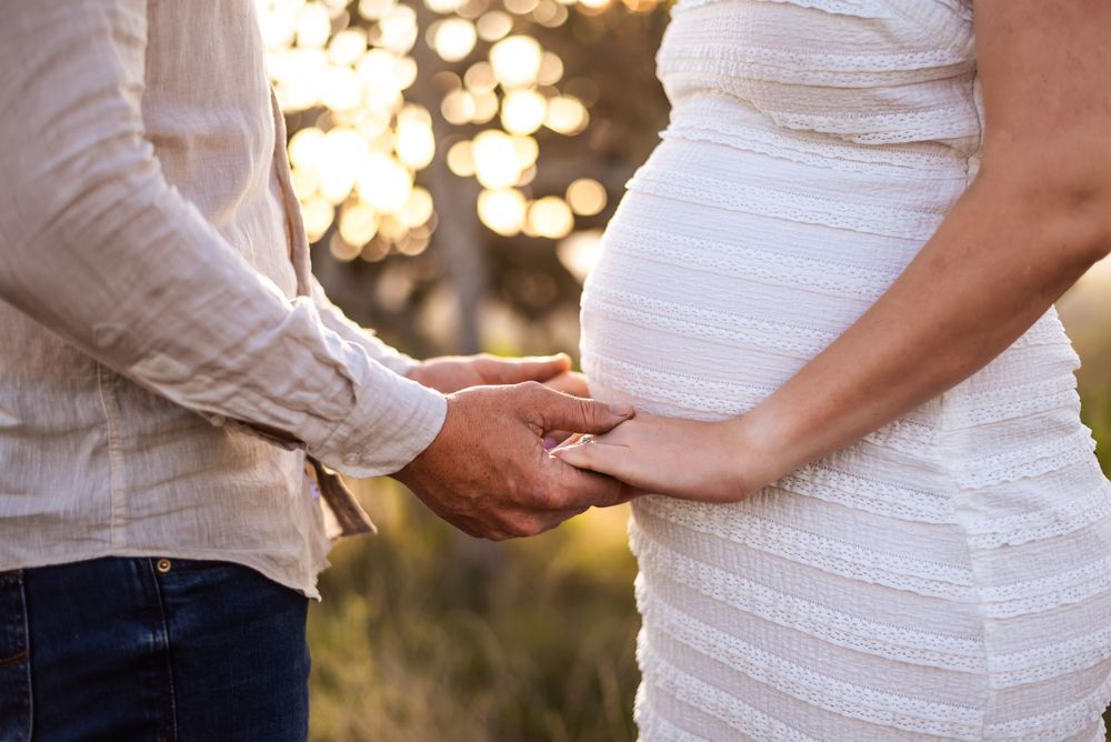 Close-up shot of hands tenderly placed on a pregnant belly in a white dress.
