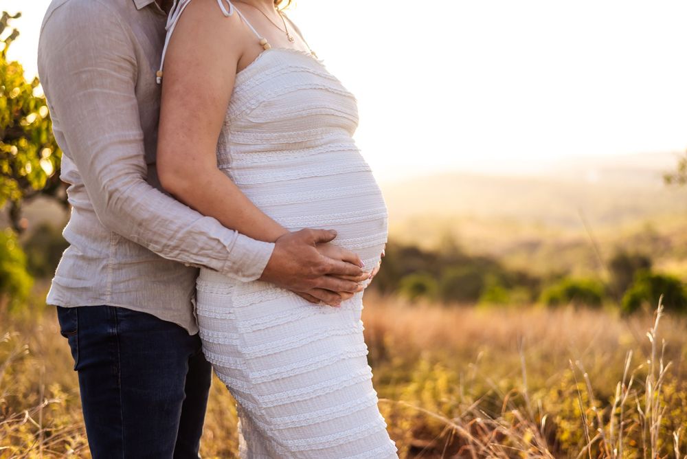 Side view of couple embracing during sunset maternity photoshoot in a field.