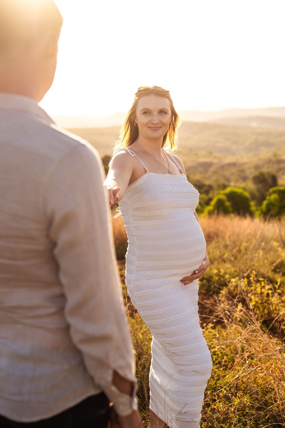 Maternity photoshoot in white dress against sunset backdrop with rolling hills.
