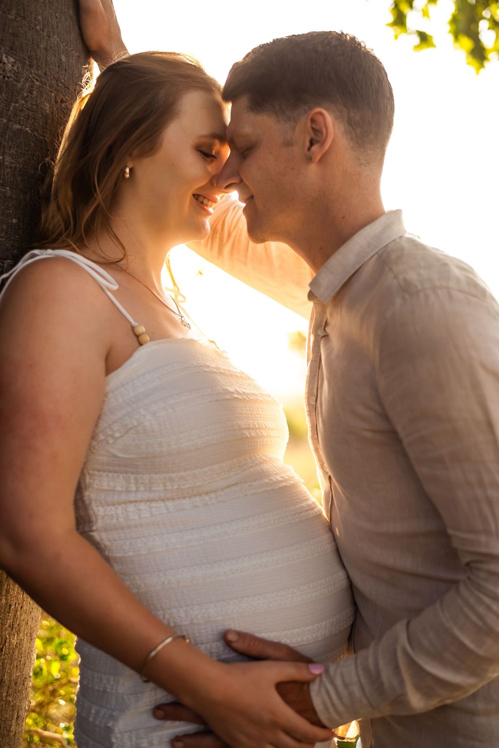Intimate maternity portrait against tree with sun flare in background.