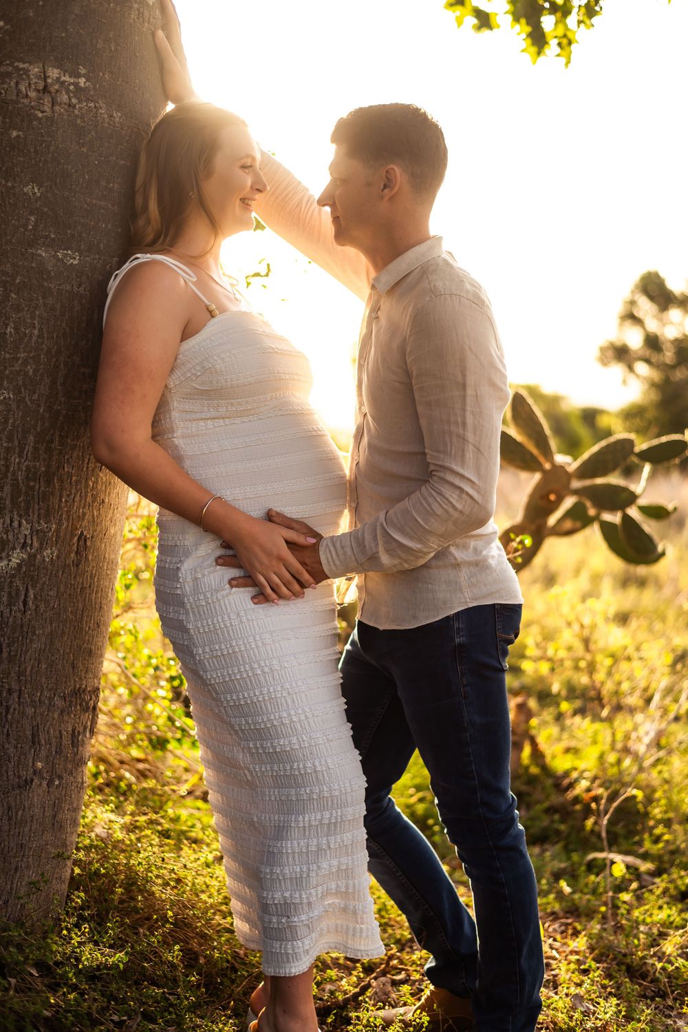 Tender moment between couple during outdoor maternity photoshoot at sunset.