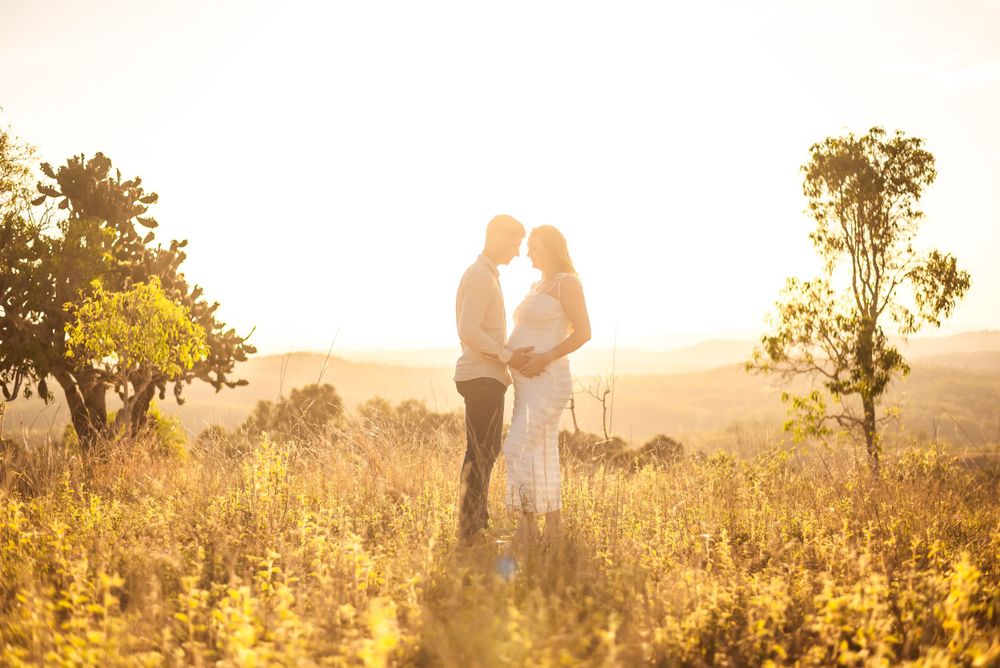 Silhouetted couple embracing in sunlit field during maternity photoshoot.