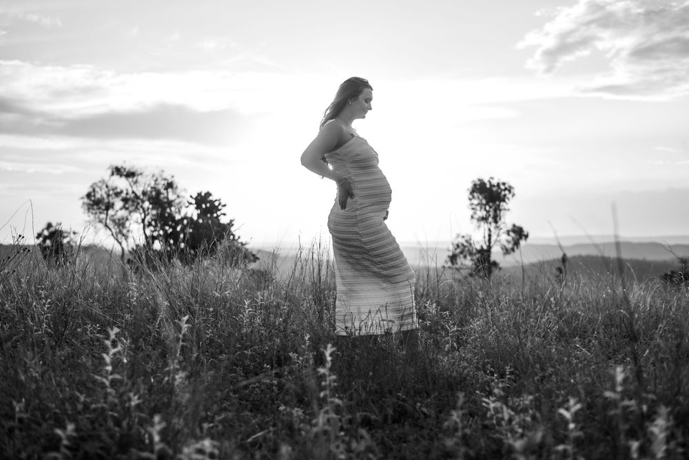 Black and white maternity portrait of woman in flowing dress standing in wildflower field.