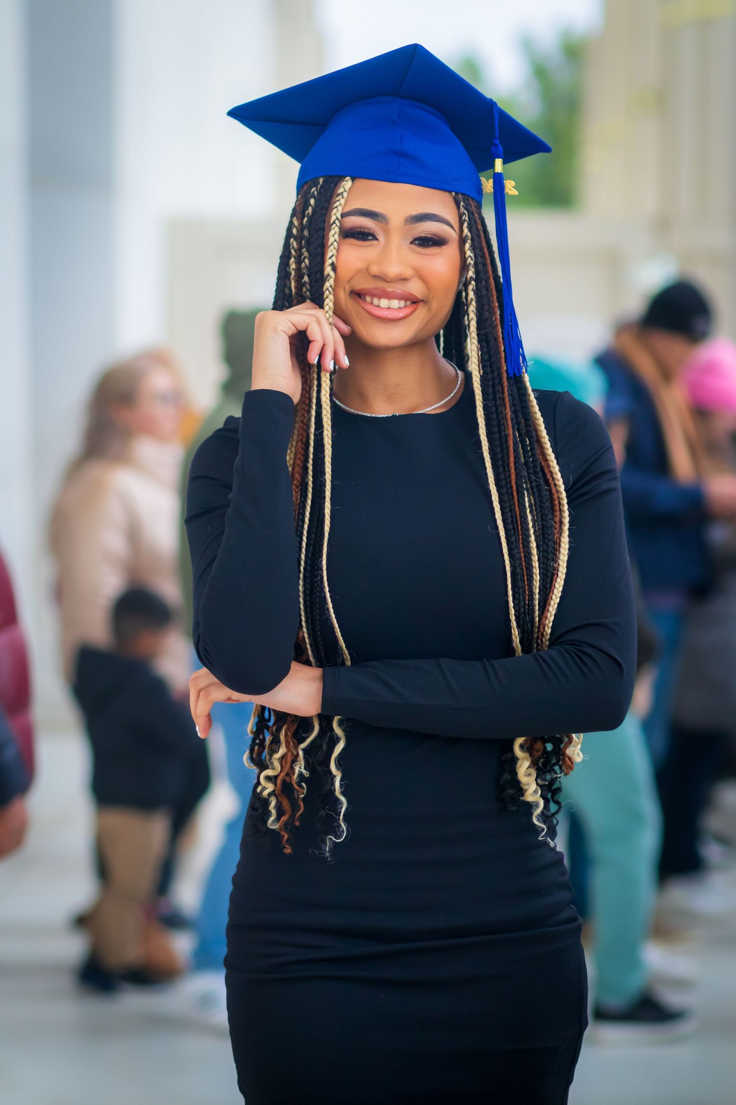 A graduation portrait featuring a black dress and blue cap with long braided hair.