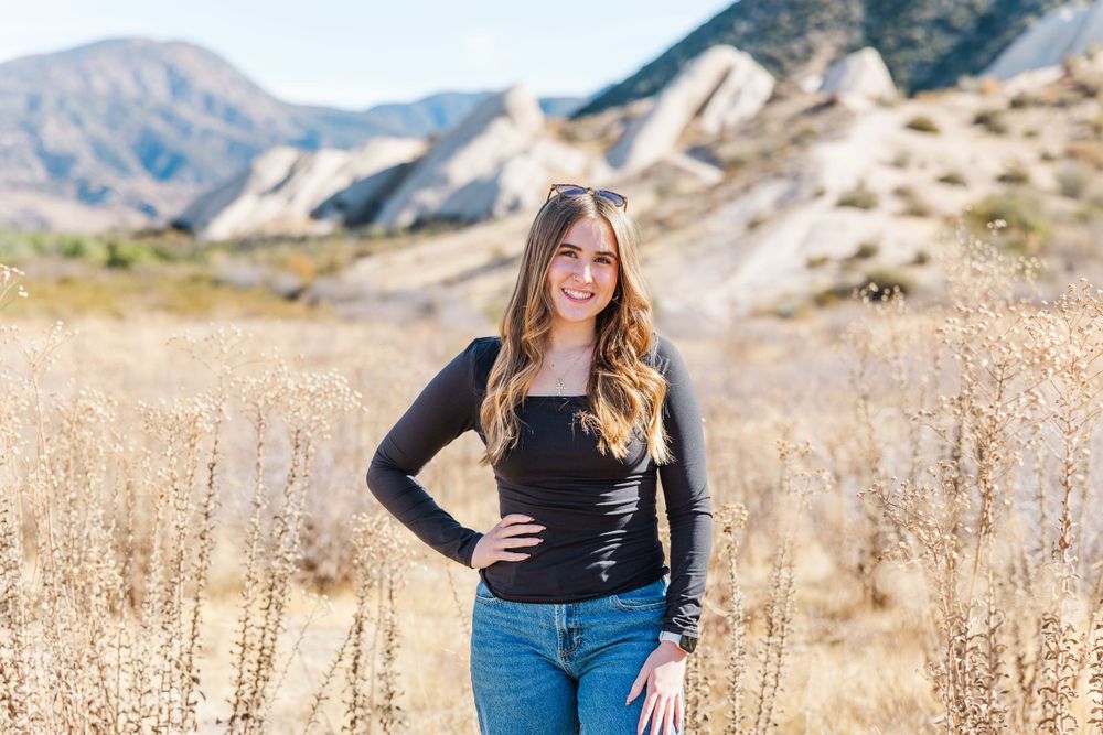 Portrait in mountain landscape with dry grass and rocky terrain in background.