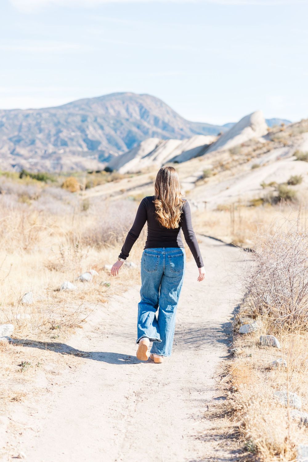 Person walking on dirt path through golden grass with mountain vista behind.