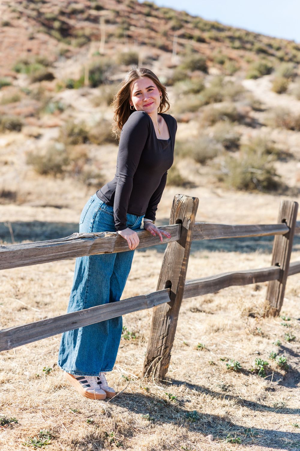 Casual portrait leaning on wooden fence with desert hills in background.