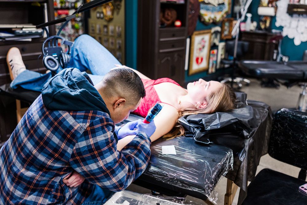 Tattoo artist works on client lying on black padded table in studio setting.