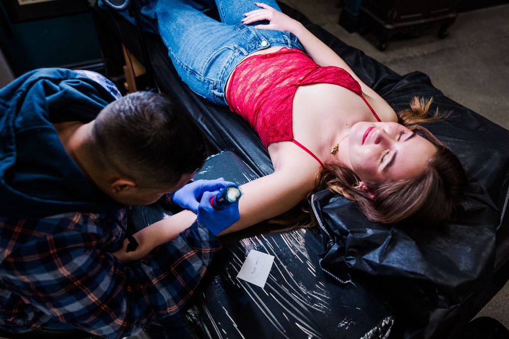 Professional tattoo session in progress with client reclining on black table.