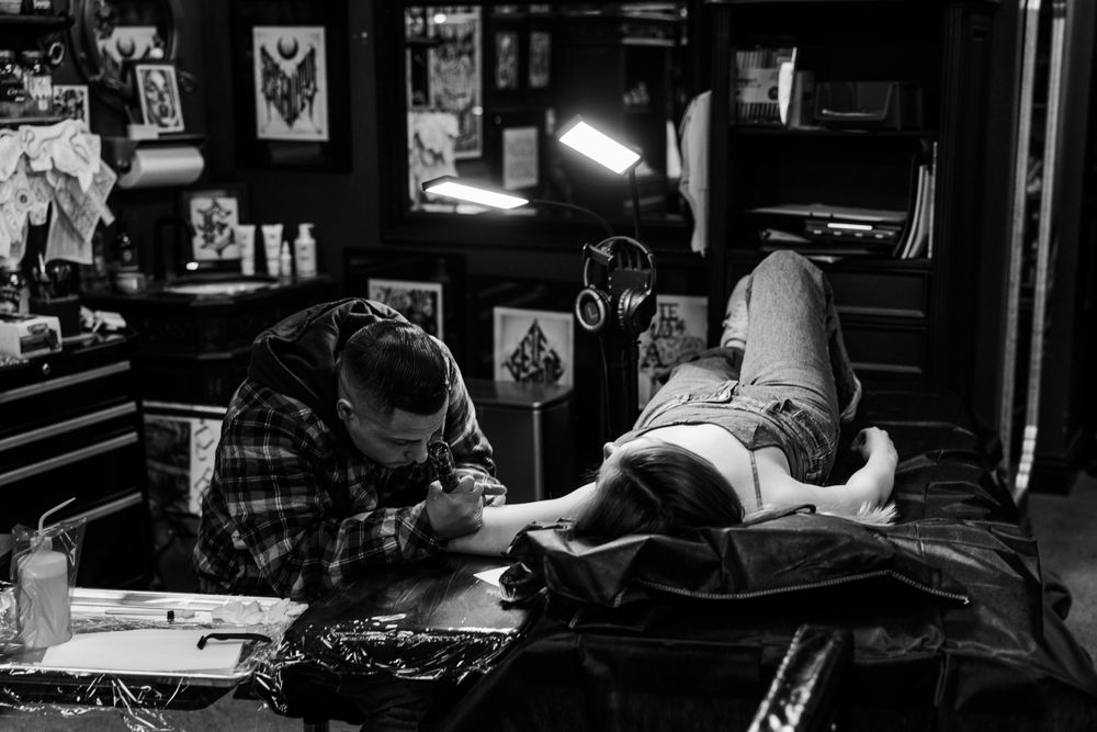 Black and white photograph of tattoo session in progress at artistic studio.